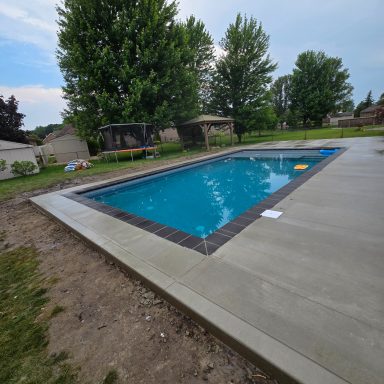 Rectangular swimming pool surrounded by a concrete deck and green lawn.