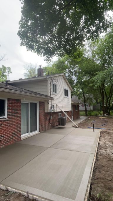 Backyard view showing a house with a concrete patio and nearby trees.