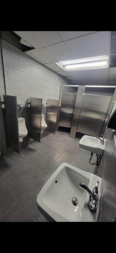 Public restroom with multiple stalls, a sink, and stainless steel fixtures.