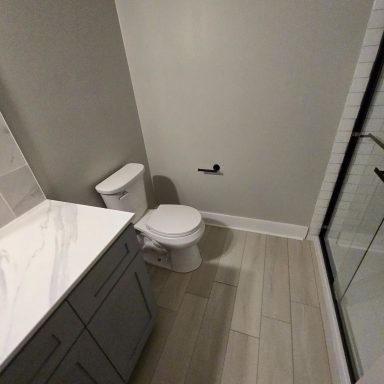 Modern bathroom with a tiled floor, toilet, vinyl floor and glass shower enclosure.