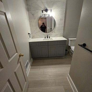 Modern bathroom featuring a circular mirror, sink cabinet, and vinyl flooring.